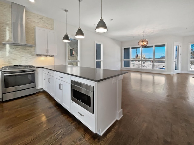 kitchen with decorative light fixtures, white cabinets, dark hardwood / wood-style flooring, stainless steel appliances, and wall chimney range hood