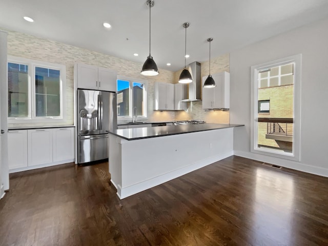 kitchen with white cabinetry, wall chimney range hood, decorative light fixtures, and stainless steel refrigerator with ice dispenser