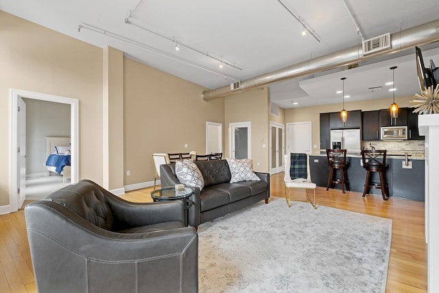 living room featuring a towering ceiling, track lighting, and light hardwood / wood-style floors