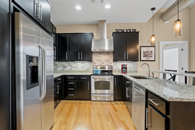 kitchen featuring decorative light fixtures, sink, stainless steel appliances, wall chimney range hood, and light hardwood / wood-style flooring