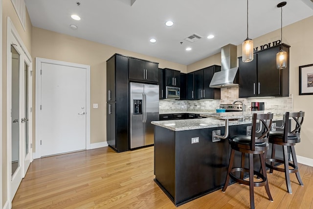 kitchen with a kitchen bar, decorative light fixtures, stainless steel appliances, light stone countertops, and wall chimney range hood