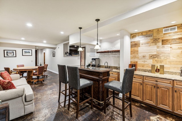 bar with hanging light fixtures, sink, and light stone counters