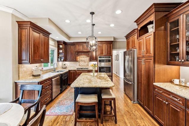 kitchen featuring sink, stainless steel appliances, a center island, light stone counters, and decorative light fixtures