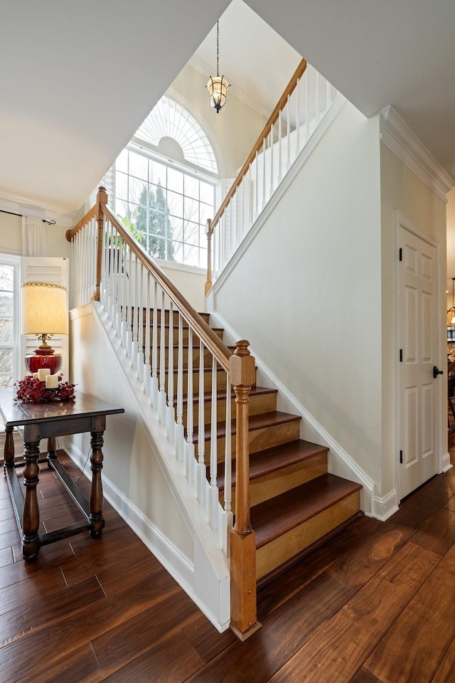 stairway featuring crown molding, wood-type flooring, and a towering ceiling