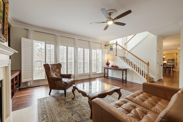 living room featuring dark wood-type flooring, ceiling fan, a premium fireplace, and crown molding