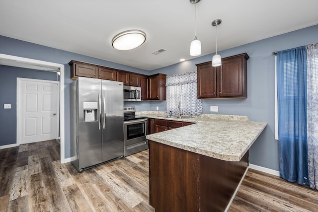 kitchen with pendant lighting, hardwood / wood-style flooring, kitchen peninsula, and appliances with stainless steel finishes