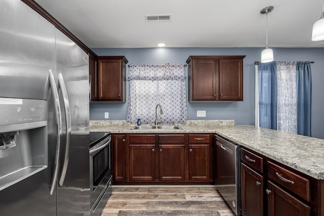 kitchen featuring sink, light hardwood / wood-style flooring, appliances with stainless steel finishes, decorative light fixtures, and kitchen peninsula