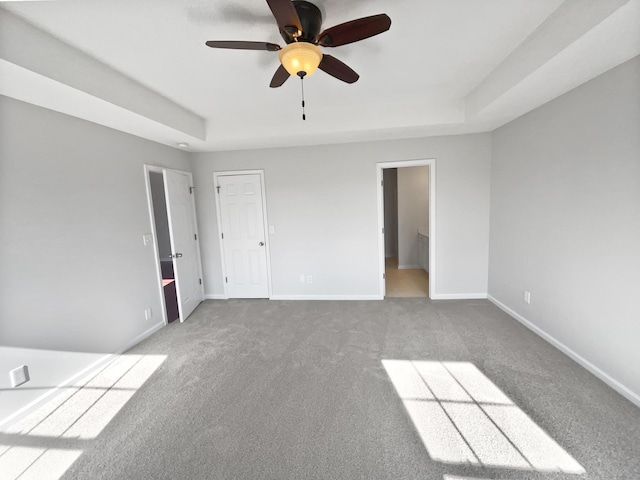 unfurnished bedroom with connected bathroom, a tray ceiling, ceiling fan, and carpet