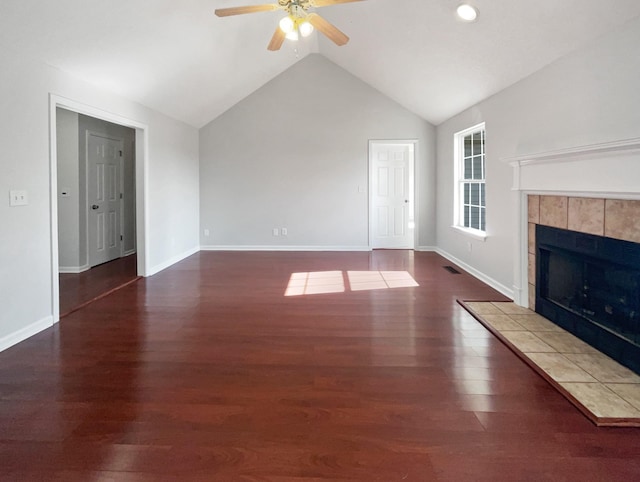 unfurnished living room with a tiled fireplace, dark wood-type flooring, lofted ceiling, and ceiling fan