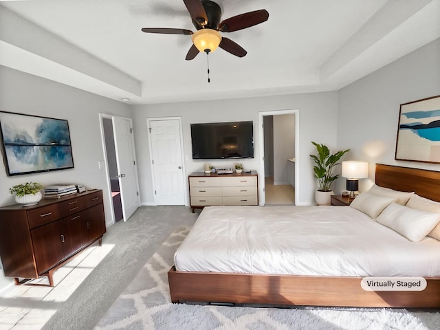 bedroom with light carpet, connected bathroom, a tray ceiling, and ceiling fan