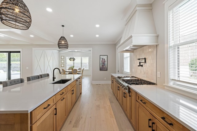 kitchen featuring sink, light hardwood / wood-style flooring, hanging light fixtures, custom exhaust hood, and a large island with sink