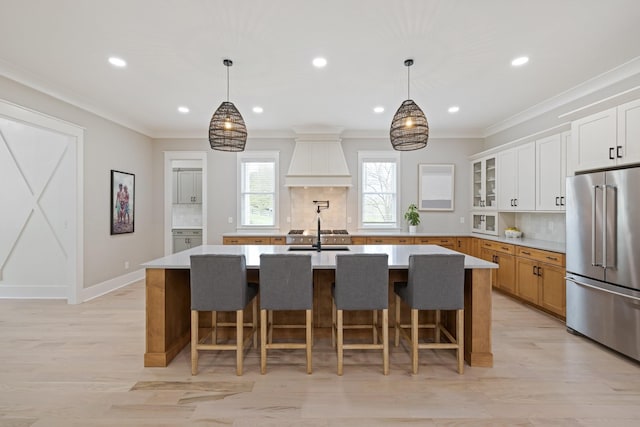 kitchen with premium range hood, high end refrigerator, a center island with sink, and white cabinets