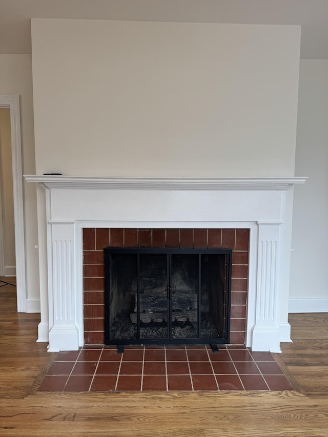 details featuring a tiled fireplace, wood finished floors, and baseboards