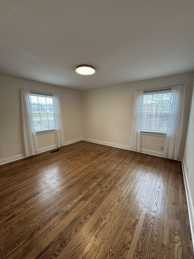 empty room with dark wood-style floors, visible vents, and baseboards