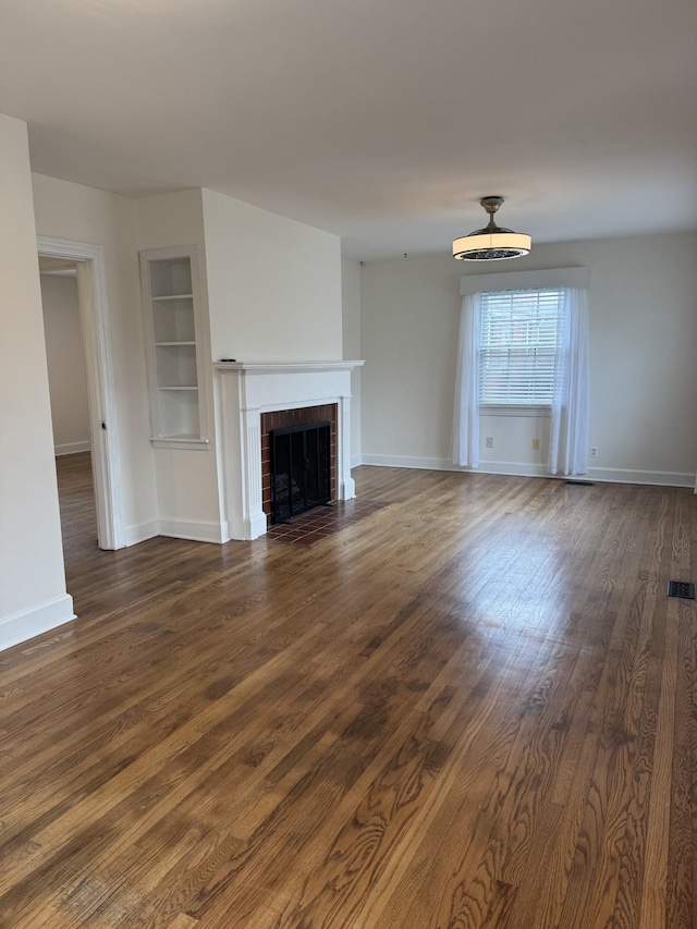 unfurnished living room featuring built in shelves, a fireplace, baseboards, and dark wood-type flooring