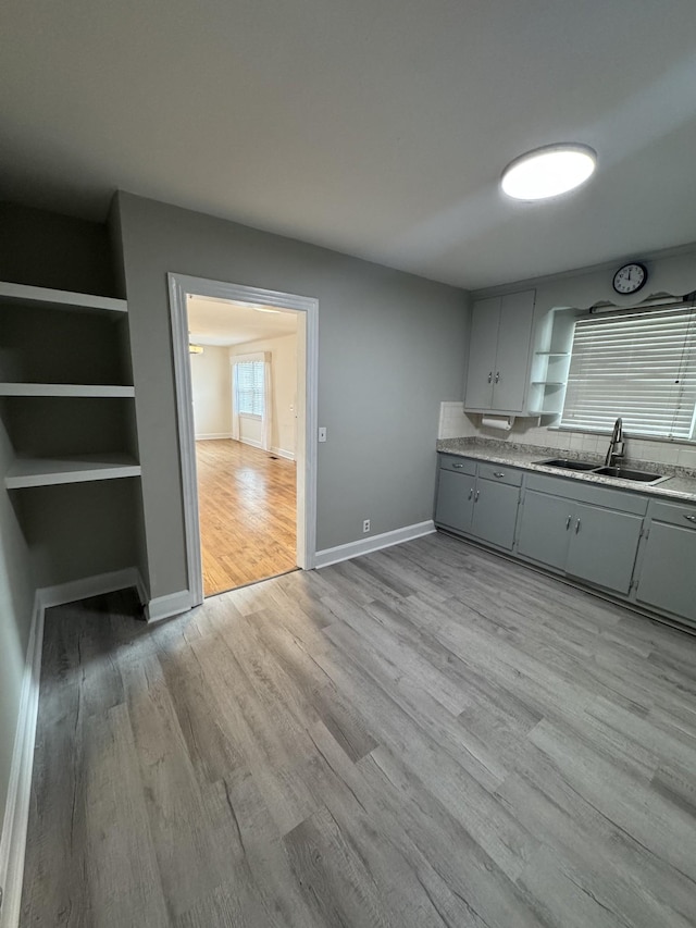 kitchen with a sink, baseboards, gray cabinets, open shelves, and light wood finished floors