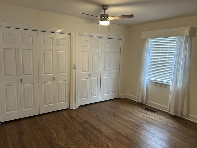 unfurnished bedroom with dark wood finished floors, two closets, visible vents, a ceiling fan, and baseboards