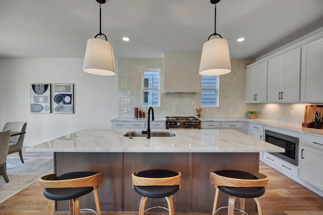 kitchen with built in microwave, high end stainless steel range, sink, a kitchen island with sink, and white cabinets