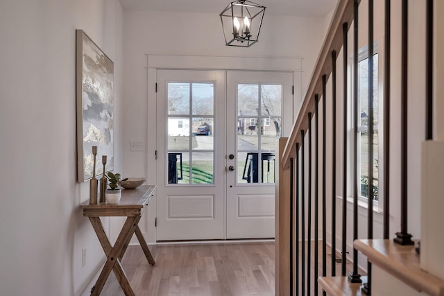 doorway to outside featuring a chandelier, a wealth of natural light, light hardwood / wood-style floors, and french doors