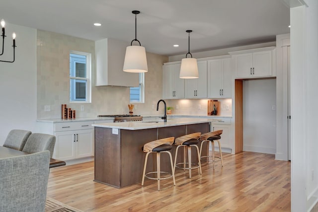 kitchen with white cabinetry, sink, decorative light fixtures, and a kitchen island with sink