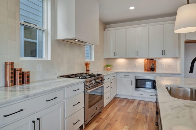 kitchen featuring sink, white cabinetry, appliances with stainless steel finishes, custom range hood, and pendant lighting