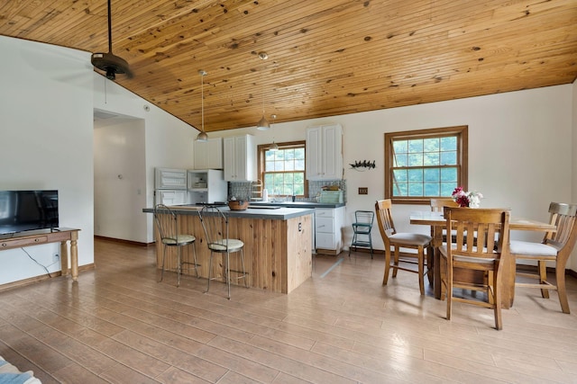 kitchen with tasteful backsplash, a breakfast bar area, white cabinets, wood ceiling, and light wood-type flooring