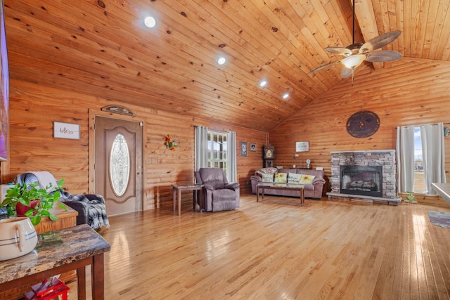 living room featuring wood ceiling, high vaulted ceiling, wooden walls, a fireplace, and light hardwood / wood-style floors