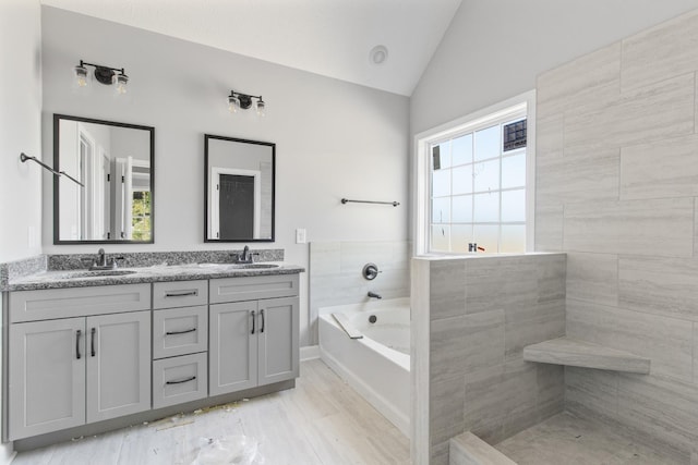 bathroom with lofted ceiling, a garden tub, a sink, and double vanity