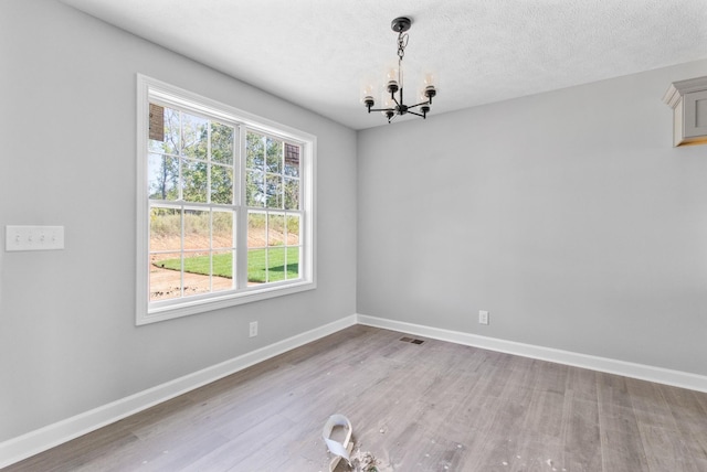 unfurnished dining area featuring visible vents, baseboards, an inviting chandelier, a textured ceiling, and light wood-style floors