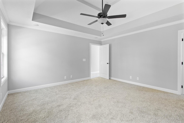 carpeted empty room with crown molding, a tray ceiling, a ceiling fan, and baseboards