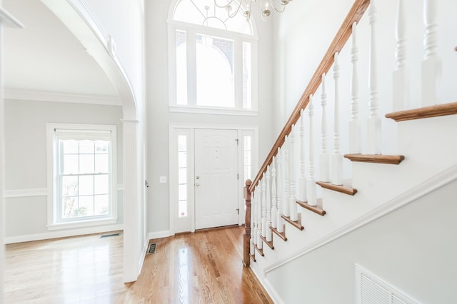 foyer with a towering ceiling, ornamental molding, light hardwood / wood-style floors, and a notable chandelier