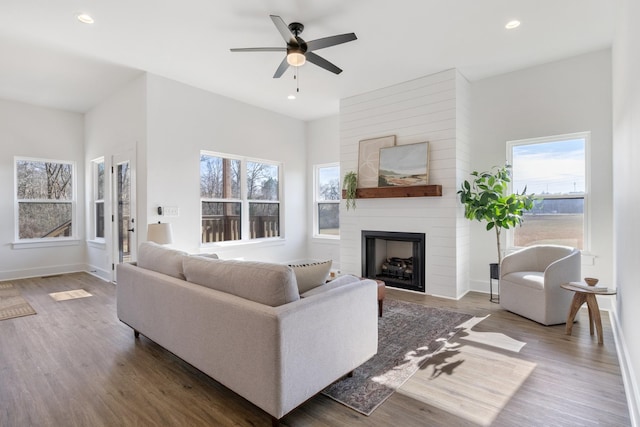 living room featuring dark hardwood / wood-style flooring, ceiling fan, a large fireplace, and a healthy amount of sunlight