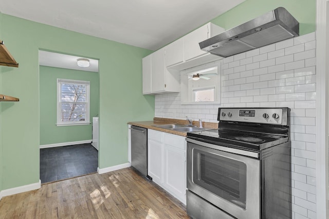 kitchen with sink, white cabinetry, light wood-type flooring, appliances with stainless steel finishes, and wall chimney range hood