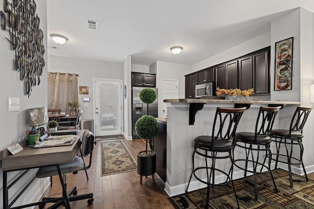 kitchen featuring dark hardwood / wood-style flooring, a kitchen breakfast bar, kitchen peninsula, stainless steel appliances, and dark brown cabinets