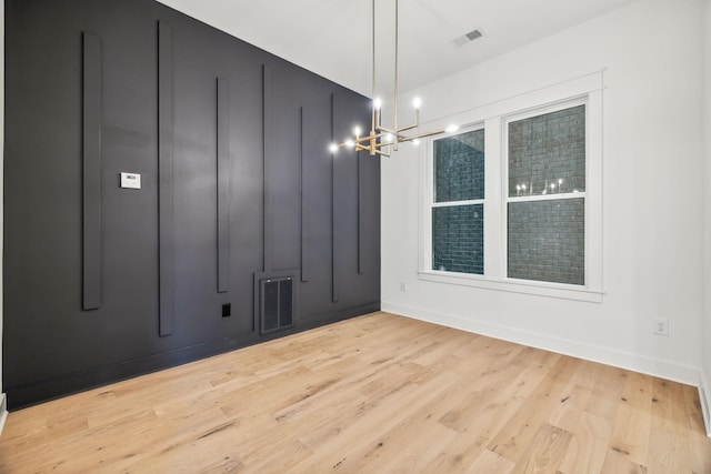 unfurnished room featuring an inviting chandelier and light hardwood / wood-style flooring