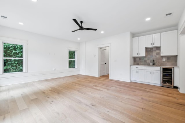 kitchen with tasteful backsplash, sink, white cabinets, beverage cooler, and light hardwood / wood-style flooring