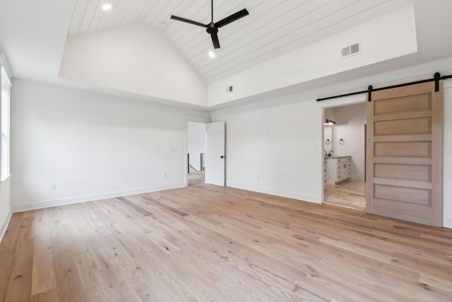 unfurnished bedroom featuring high vaulted ceiling, wood ceiling, light hardwood / wood-style floors, a barn door, and ensuite bath