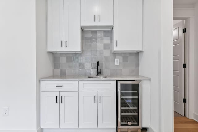 bar with sink, white cabinetry, wine cooler, tasteful backsplash, and light stone counters