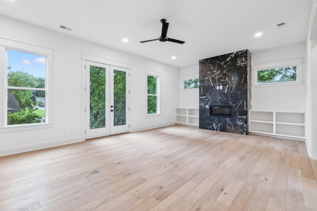 unfurnished living room featuring a wealth of natural light, light hardwood / wood-style floors, a premium fireplace, and ceiling fan