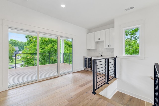 kitchen with sink, white cabinetry, beverage cooler, light hardwood / wood-style floors, and backsplash