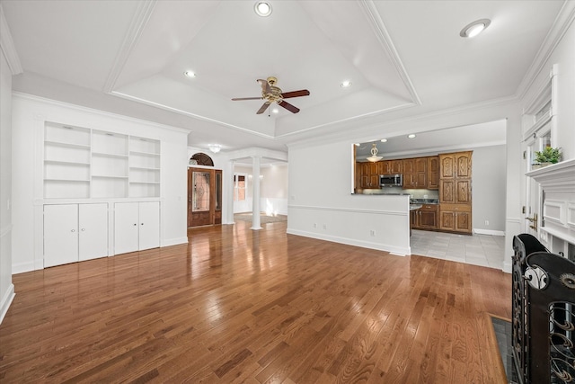 living room with crown molding, a raised ceiling, light hardwood / wood-style flooring, and ornate columns