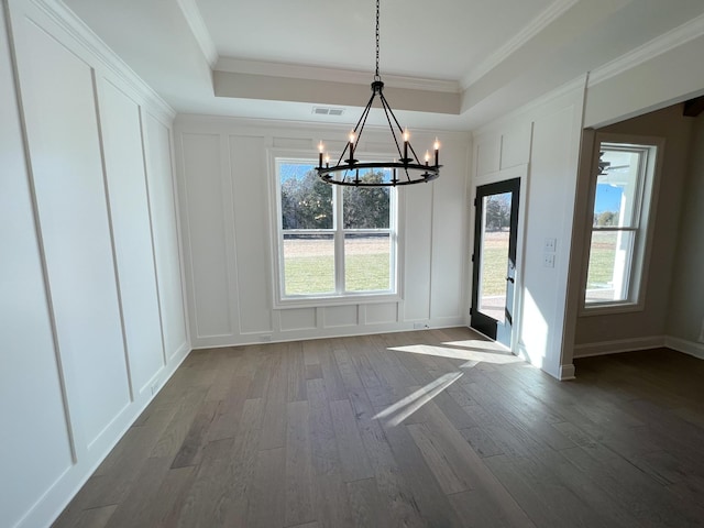 unfurnished dining area featuring dark wood-style floors, a tray ceiling, a chandelier, and a decorative wall