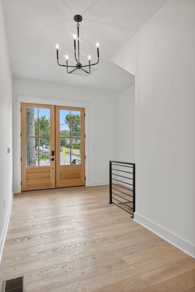 unfurnished dining area with an inviting chandelier, light hardwood / wood-style floors, and french doors