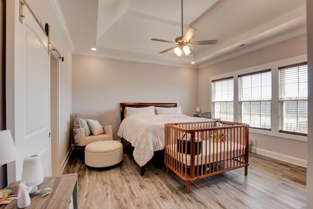 bedroom featuring a raised ceiling, light wood-style flooring, and a barn door