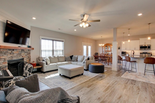 living area with a toaster, recessed lighting, a stone fireplace, light wood-style floors, and ceiling fan with notable chandelier