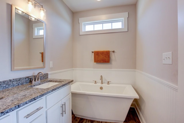 bathroom with a soaking tub, wainscoting, vanity, and a healthy amount of sunlight