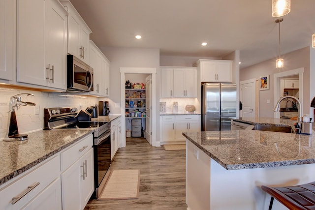 kitchen with dark stone countertops, stainless steel appliances, light wood-type flooring, white cabinetry, and a sink