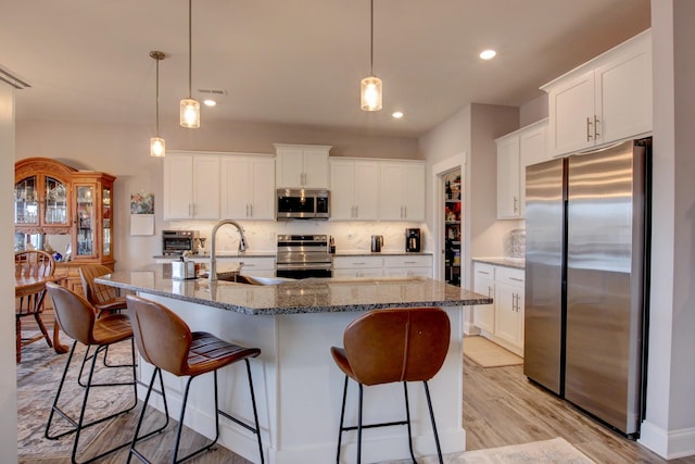 kitchen with a breakfast bar area, light wood finished floors, stainless steel appliances, backsplash, and a sink