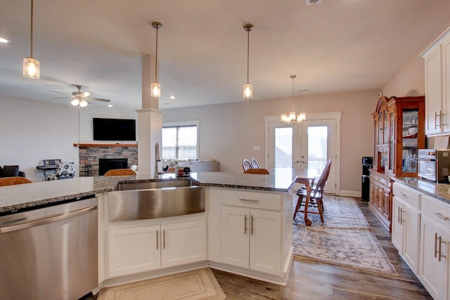 kitchen featuring wood finished floors, stainless steel dishwasher, stone counters, a fireplace, and a sink