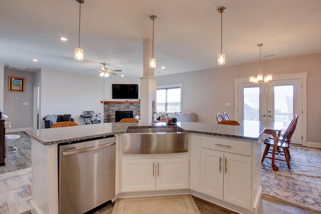 kitchen with a stone fireplace, a sink, open floor plan, light stone countertops, and dishwasher